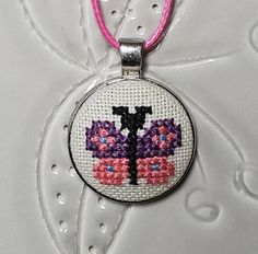 a cross stitched pendant with pink and purple flowers on it's front end