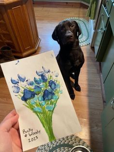 a black dog sitting on the floor next to a card with blue flowers in it