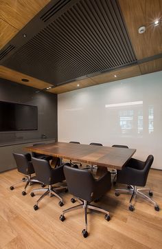 an empty conference room with black chairs and a wooden table in front of a flat screen tv