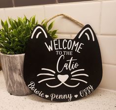 a black cat sign sitting on top of a counter next to a potted plant