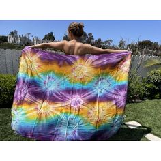 a woman is wrapped up in a colorful tie - dyed blanket while standing on the grass