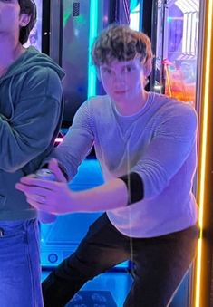 two young men standing next to each other in front of a tv screen with neon lights