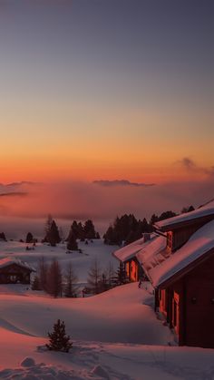 the sun is setting over a snowy landscape with mountains in the distance and houses on either side