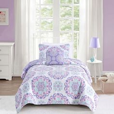 a purple and white bed in a bedroom next to a window with two lamps on either side