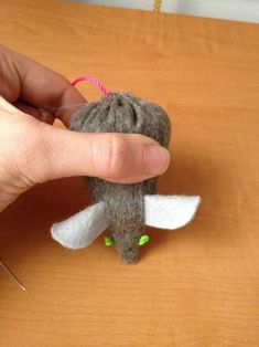 a hand is holding a small stuffed animal with green eyes and white tail, on top of a wooden table