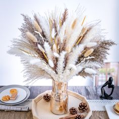 a glass vase filled with feathers sitting on top of a wooden tray next to pine cones