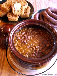 there is a bowl of beans next to bread and hotdogs on the table