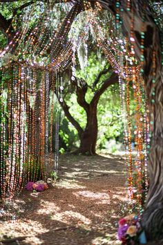 an outdoor wedding ceremony with beads hanging from the trees and flowers on the ground in front of it