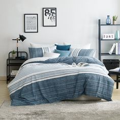 a bed with blue and white striped comforter in a living room next to a book shelf