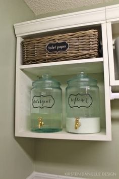 two jars with labels on them are sitting in a shelf above a toilet paper dispenser