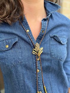 a woman wearing a denim shirt with a gold pineapple pendant on it's neck