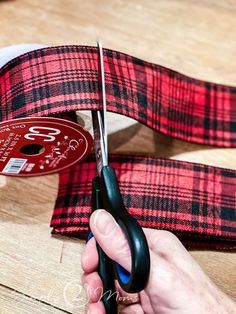 a person cutting fabric with scissors on top of a wooden table next to some tape