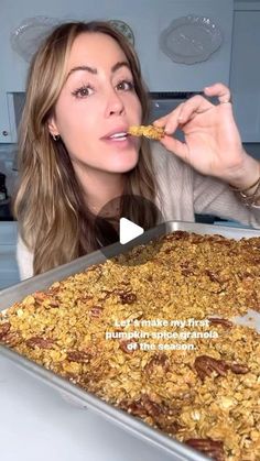 a woman eating granola from a pan in the kitchen while looking at the camera