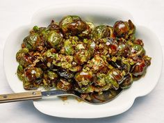 a white bowl filled with cooked brussel sprouts next to a wooden spoon