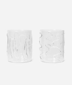 two clear glass cups sitting next to each other on a white surface, one is empty and the other has no lid