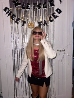 a woman wearing sunglasses standing in front of a door with streamers on the wall