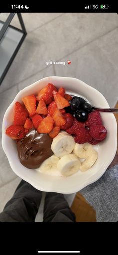 a person holding a bowl full of fruit and nutella with chocolate sauce on top