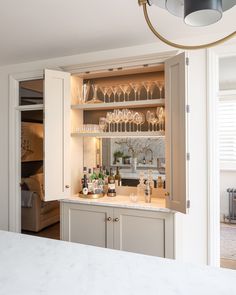 an open cabinet with wine glasses and bottles on it in a kitchen next to a bar