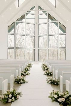 the aisle is decorated with white flowers and greenery as well as candles in front of large windows