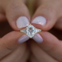 a woman's hands holding a ring with an oval shaped diamond on it and two smaller diamonds in the middle