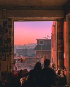 two people looking out an open window at the city below and pink sky in the distance