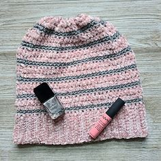 a pink and gray hat with lipstick next to it on top of a wooden table