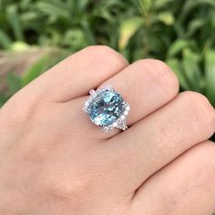 a woman's hand holding an aqua blue and white ring with diamonds on it