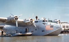 an airplane with people standing on top of it sitting in the water next to another plane