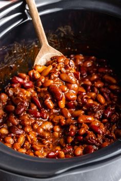 the beans are being cooked in the crock pot with a wooden spoon to stir them