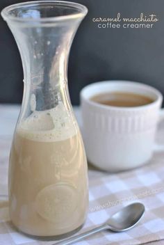 a glass pitcher filled with liquid next to a cup of coffee on a checkered tablecloth