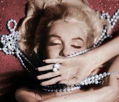 a woman wearing pearls is hugging another woman's face with her hands on her chest