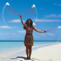 a woman is standing on the beach and juggling balls in her hands while wearing a skirt