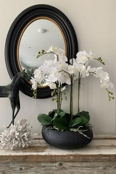 white flowers in a black vase on a table next to a mirror and horse figurine