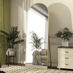 a large mirror sitting on top of a wooden floor next to a white dresser and potted plant