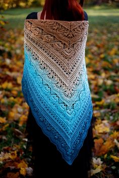 a woman is standing in the leaves wearing a blue and white crocheted shawl