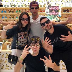 three people posing for a photo with their hands up in front of them and bananas on the wall behind them