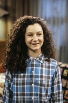 a woman with curly hair is smiling at the camera while wearing a blue and black plaid shirt