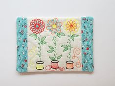 an embroidered wallet with flowers and coffee mugs on the front, sitting on a white surface