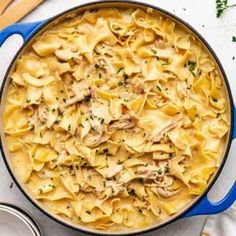 a blue pot filled with pasta covered in chicken and sauce on top of a white table