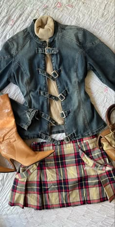 a denim jacket and plaid skirt are laid out on a bed with high heel boots