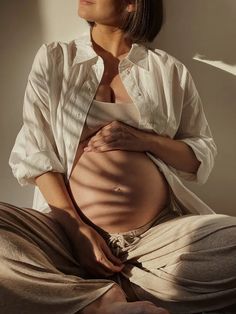 a pregnant woman sitting on the floor with her hands in her stomach and looking up