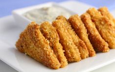 some fried food on a white plate next to a small bowl of dip and sauce