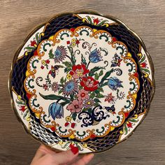 a hand holding a decorative plate on top of a wooden table next to a wall