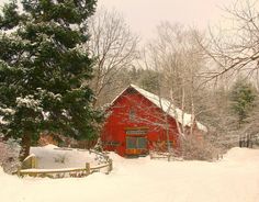 a red barn in the middle of a snow covered field with trees and fence around it