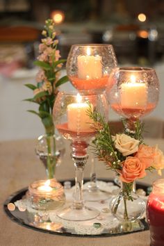 candles and flowers are sitting on a tray next to some wine glasses with roses in them