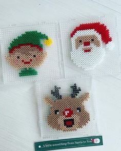 three cross stitch christmas ornaments on a white table with a green sticker in the shape of santa claus and rudolph