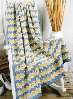 a blue and yellow crocheted blanket sitting on top of a white rocking chair