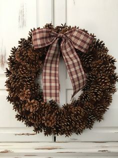 a pine cone wreath with a bow hanging on the front door, ready to be hung