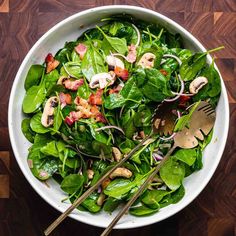 a salad with spinach, mushrooms and bacon in a white bowl on a wooden table