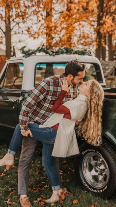 a man and woman kissing in front of an old truck with autumn leaves on the ground